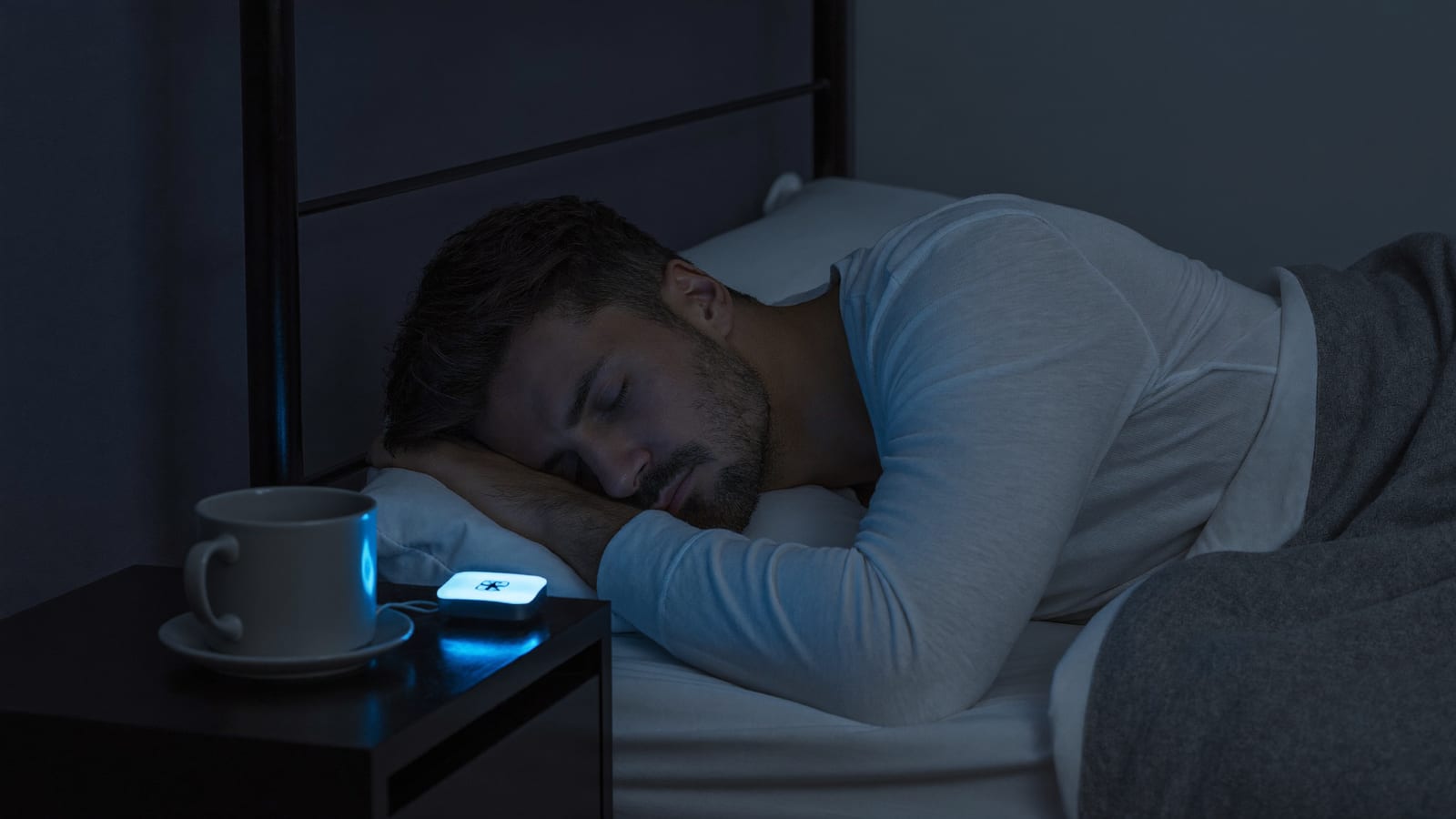 Ruhig schlafender Mann, Schlaf-Tracker leuchtet am Nachttisch